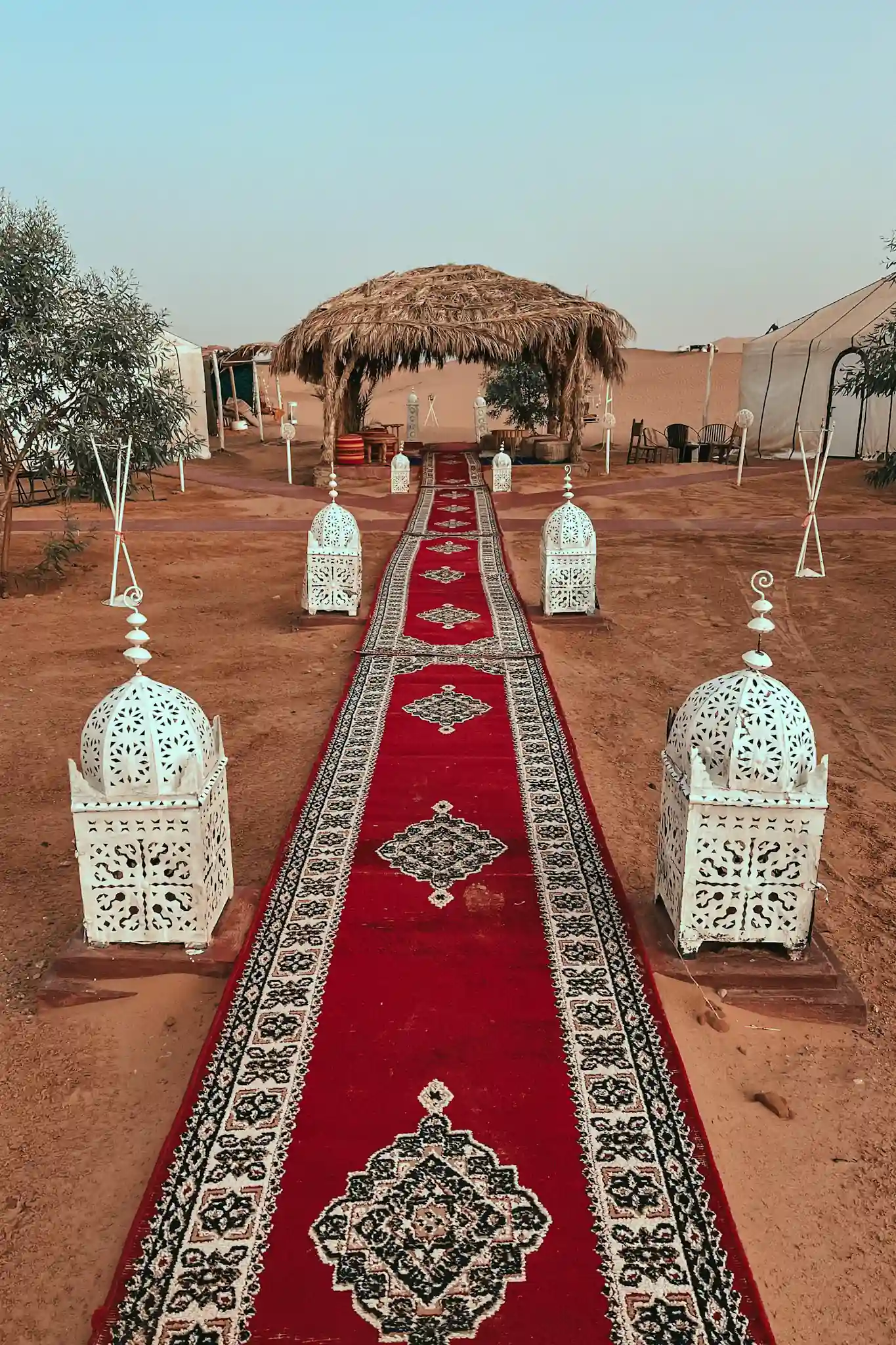 Desert camp in Merzouga with huts, lanterns, and rugs.