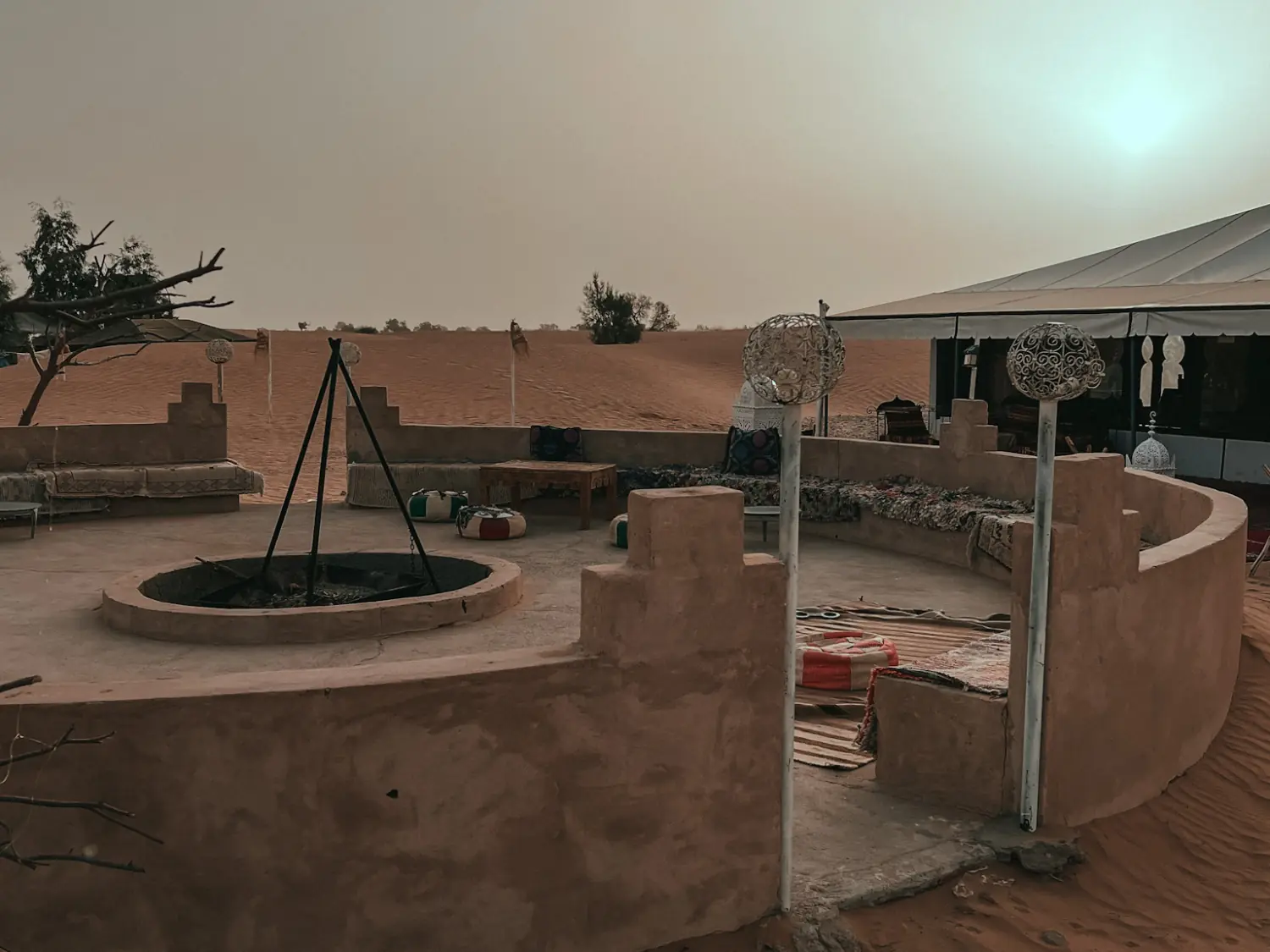 Seating area at desert camp in Merzouga with camp fire and hazy desert sky.